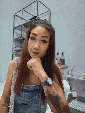 a woman wearing overalls and a watch is looking at the camera