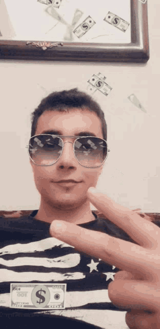 a man wearing sunglasses and a shirt with a dollar bill on it giving a peace sign