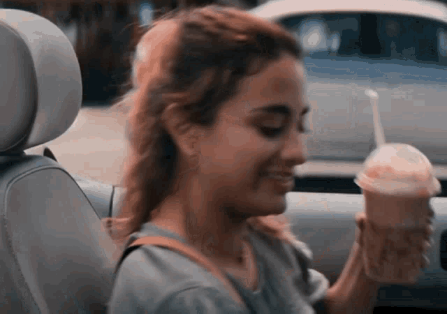 a woman sitting in a car holding a drink
