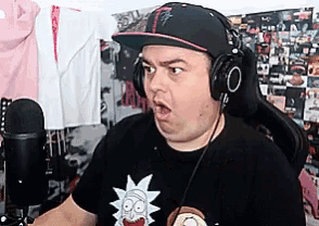a man wearing a hat and headphones is sitting in front of a microphone and making a funny face .