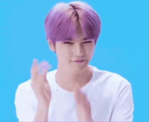 a man with purple hair and a white shirt is clapping his hands .