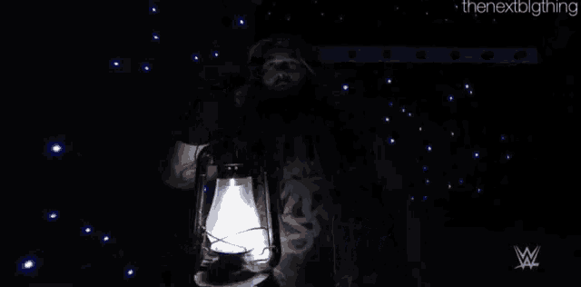 bray wyatt is holding a lantern in his hand in the dark