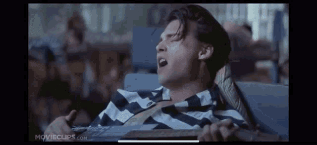 a man in a striped shirt is sitting in a chair holding a guitar and yawning .