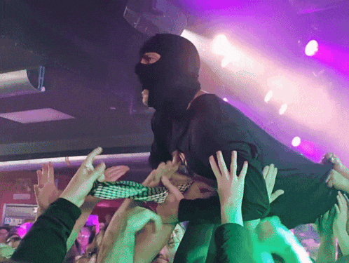 a man wearing a ski mask is being lifted in the air by a crowd