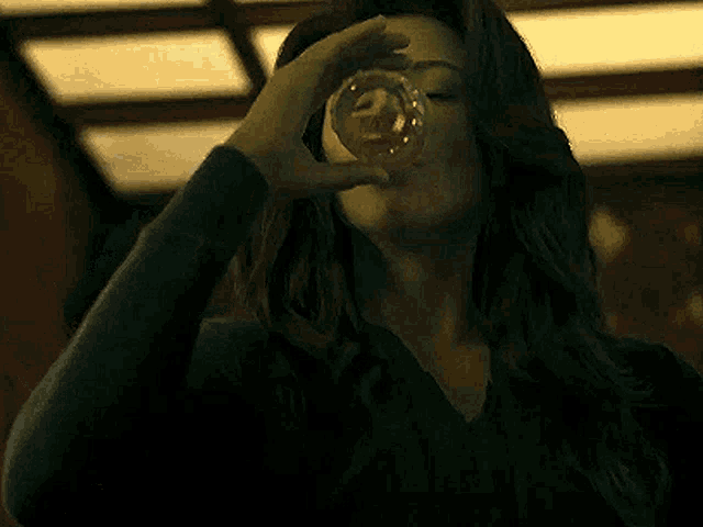 a woman is drinking from a glass while making a heart shape with her hands .