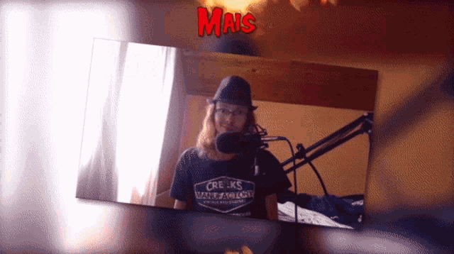 a man wearing a creek 's water factory shirt is standing in front of a microphone