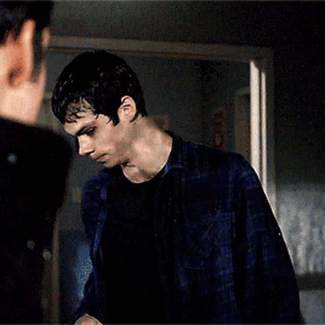 a young man in a blue plaid shirt is looking at another man