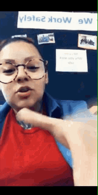 a woman wearing glasses and a red shirt is pointing at something .
