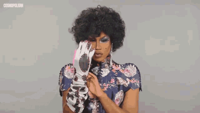 a woman in a floral top is holding a pink object and the word cosmopolitan is on the bottom right