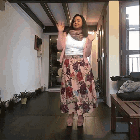 a woman wearing a floral skirt and a pink cardigan is standing in a hallway