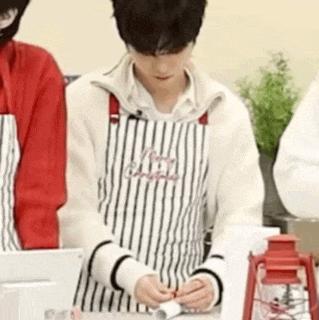 a man wearing an apron is standing in front of a table .