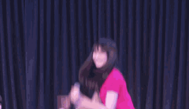 a woman in a pink shirt is dancing on a stage with her arms in the air .