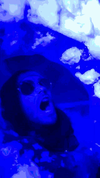 a person wearing sunglasses and a hat is screaming in a blue room