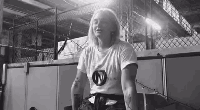 a black and white photo of a woman in a white shirt standing in a gym .