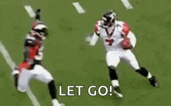 a football player is running towards another player who is laying on the ground on a field .
