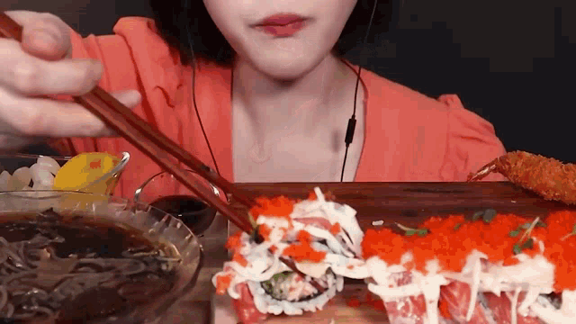 a woman is eating sushi with chopsticks while wearing ear buds