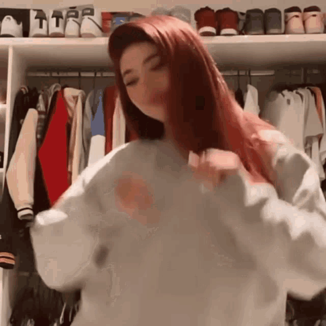 a woman with red hair is standing in front of a closet full of clothes and shoes .