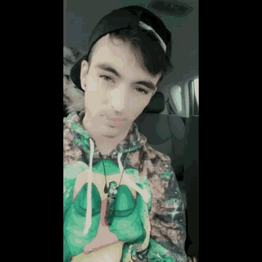 a young man wearing a hat and a colorful hoodie is sitting in the back seat of a car