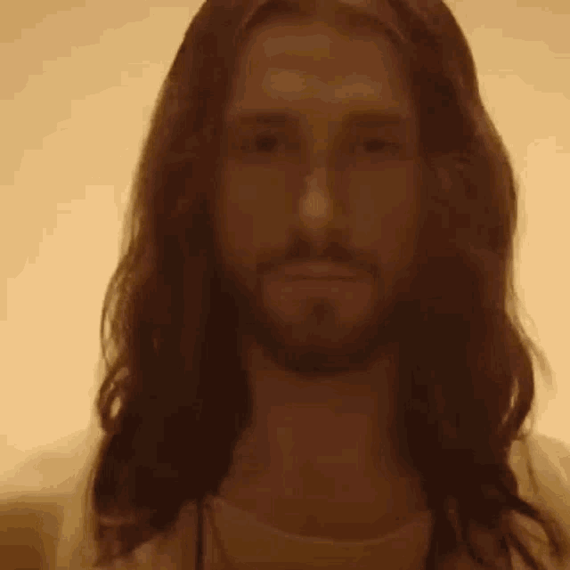 a man with long hair and a beard is looking at the camera in a dark room .