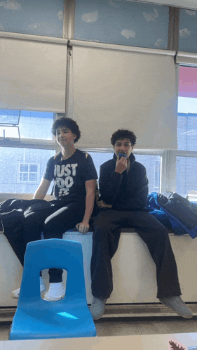 a boy wearing a just do it shirt sits next to another boy in a blue chair