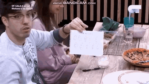 a man sitting at a table holding a piece of paper that says ' www.bandicam.com '