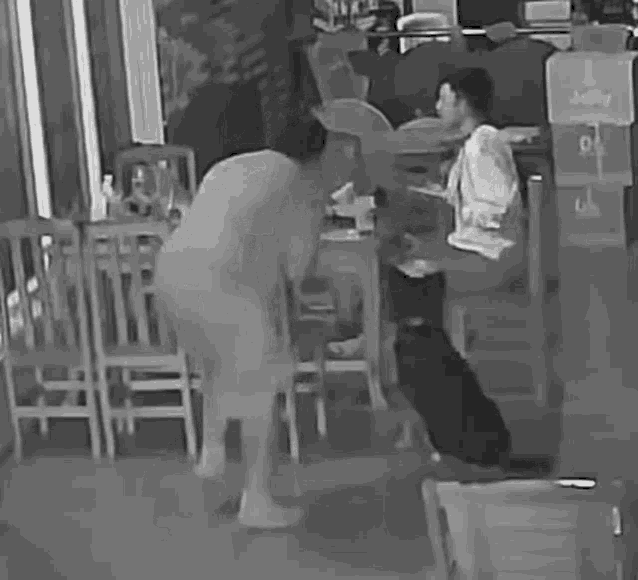 a man is standing next to a woman sitting at a table in a restaurant in a black and white photo .