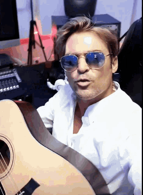a man wearing sunglasses and a white shirt is holding a guitar