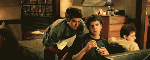 two men are looking at a computer screen and one is holding a can of soda
