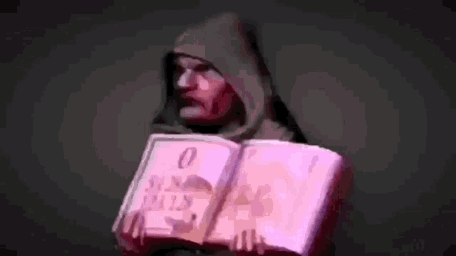 a man in a hood is holding a book in his hands in russian .