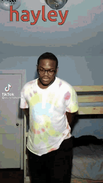a man in a tie dye shirt is standing in front of a bunk bed with the name hayley written on the ceiling