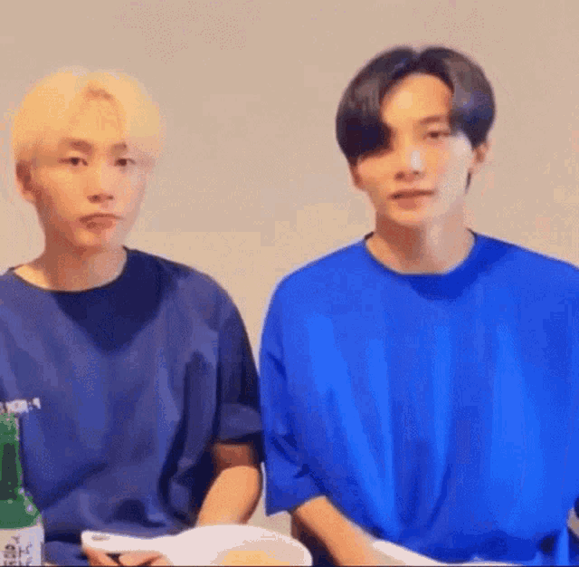 two men in blue shirts are sitting next to each other and looking at the camera .