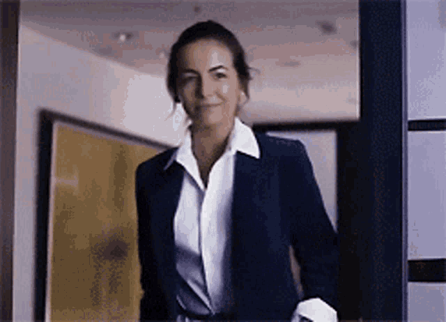 a woman in a blue jacket and white shirt is smiling in a hallway