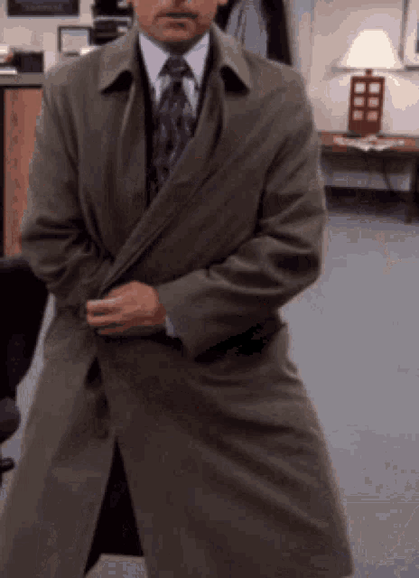 a man in a trench coat and tie is standing in an office .