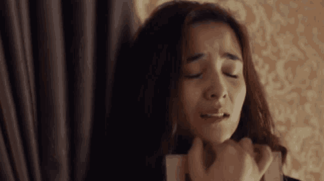 a woman is crying with her eyes closed and her hands on her face