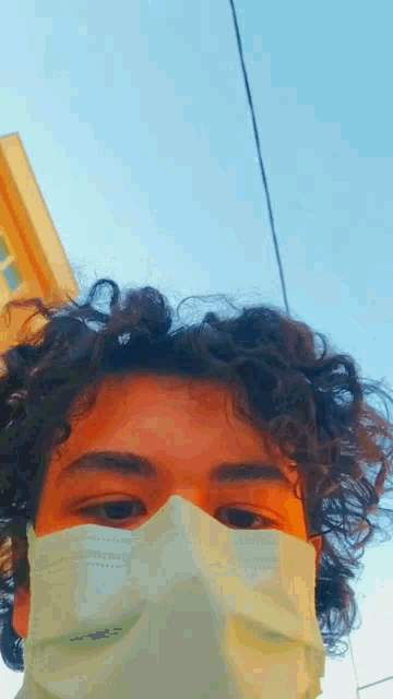 a young man with curly hair is wearing a white mask .