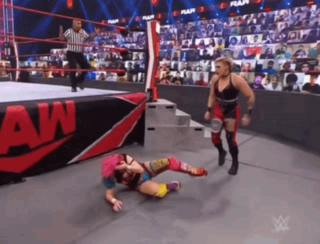 a woman is laying on the ground in a wrestling ring while a referee looks on .