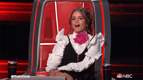 a woman with a flower in her hair is sitting in a chair with a nbc logo in the background .