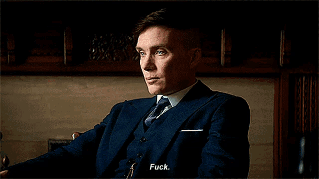 a man in a suit and tie is sitting in a chair and saying " fuck "