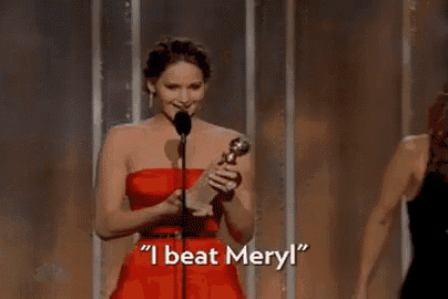 a woman in a red dress is holding a trophy and saying `` i beat meryl '' on a stage .