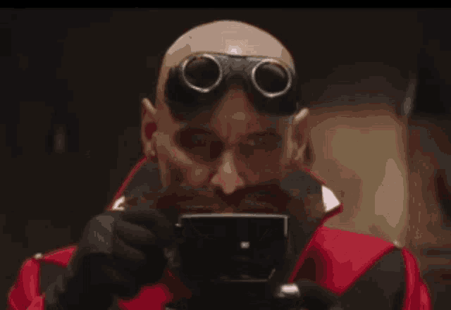 a bald man with a mustache and goggles is drinking from a cup