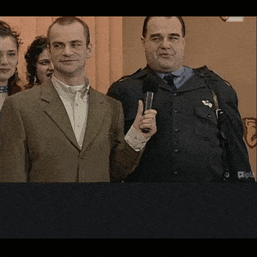 a man in a suit holds a microphone next to another man in a uniform