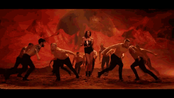 a woman in a black bodysuit is standing in the middle of a group of dancers in a dark room .
