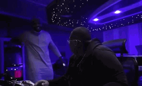 a man in a white shirt is standing next to another man in a dark room with blue lights