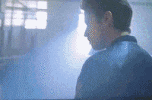 a man in a blue shirt is standing in front of a window in a room .