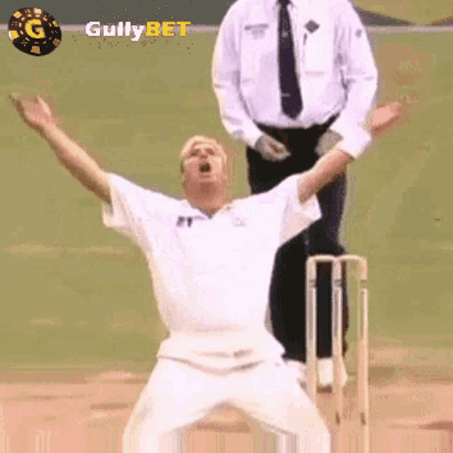 a man in a white shirt is standing on a cricket field with his arms in the air