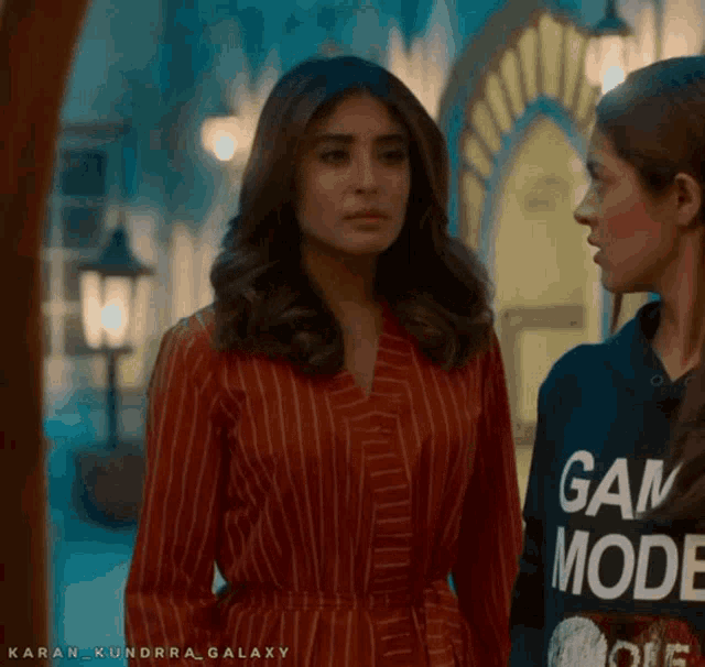 two women are standing next to each other and one is wearing a game mode sweatshirt
