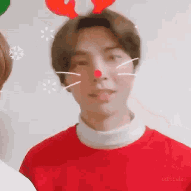 a young man wearing a red sweater and reindeer antlers is making a funny face .