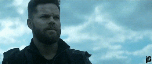 a man with a beard stands in front of a cloudy sky with the letter f on the bottom