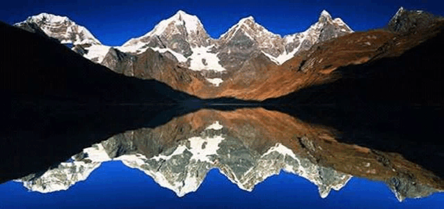 a mountain range is reflected in a lake with a blue sky in the background