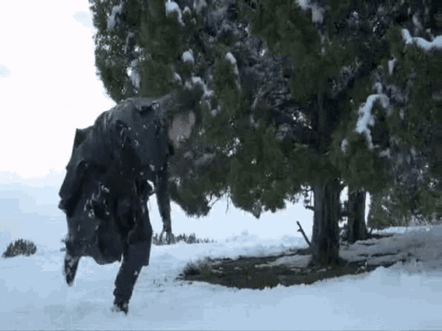 a man is running through the snow in front of a snow covered tree .
